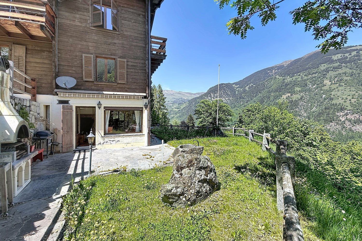 Le chalet vu du jardin : terrasse en pierres naturelles et grandes fenêtres du séjour.